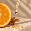 Dropper with a drop of facial serum next to an orange slice