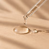 Dropper with a drop of facial serum on a beige background